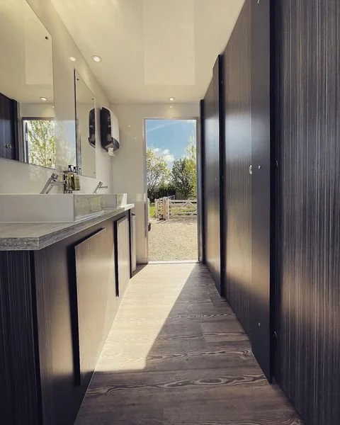 Luxury trailer hallway with natural light, vessel sinks and dark wood cubicles