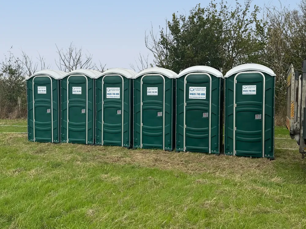 Row of six green PremierPlus portable toilets lined up on grass ready for an outdoor event