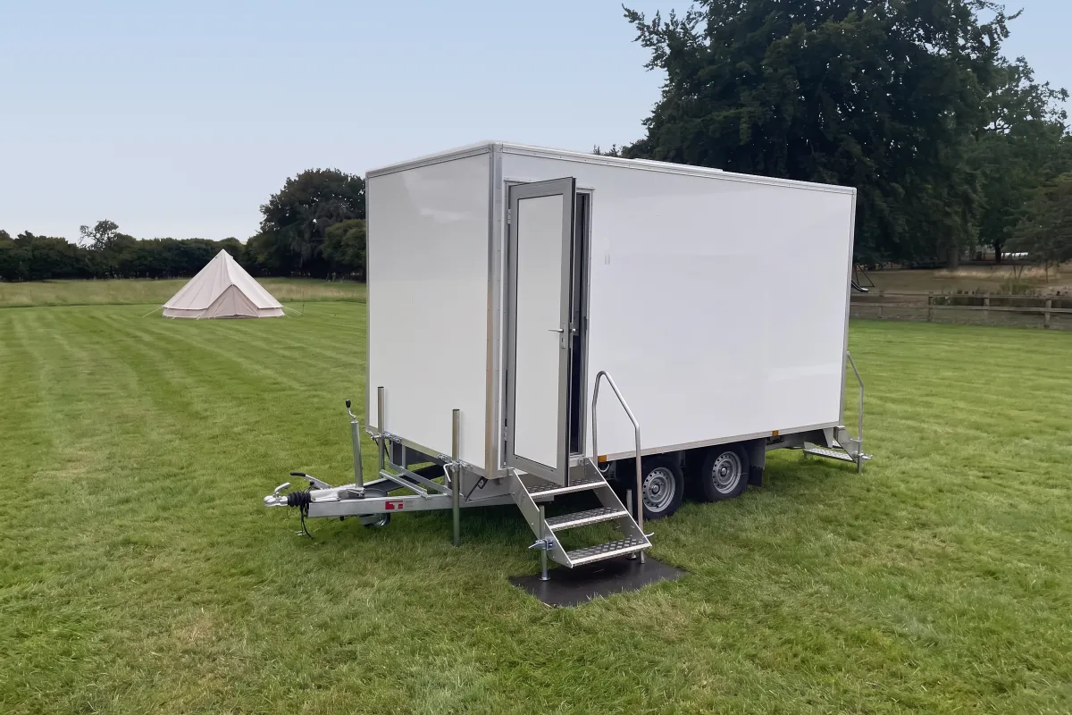 White PremierPlus toilet trailer with fold-down steps set up in a green field beside a bell tent