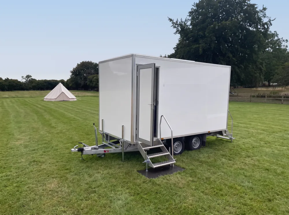 White PremierPlus toilet trailer with fold-down steps set up in a green field beside a bell tent