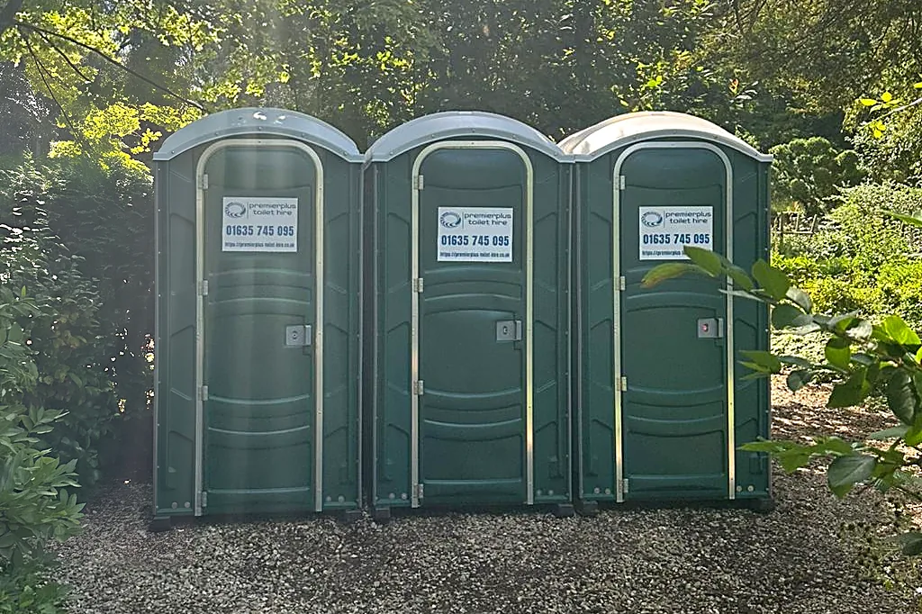 Three PremierPlus event-grade portable toilets on a gravel path in a private garden